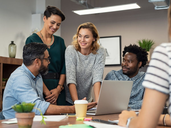 Multiethnic business people talking and smiling during meeting in office. Mature middle eastern man explaining proposal. Happy businessman showing project and marketing strategy on laptop to colleague