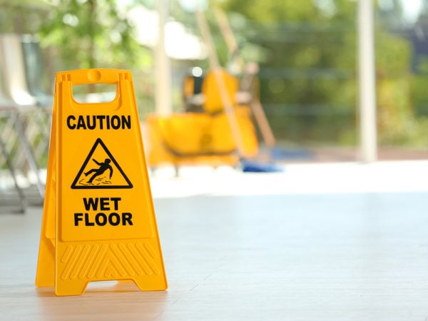 Safety sign with phrase Caution wet floor and blurred mop bucket on background. Cleaning service