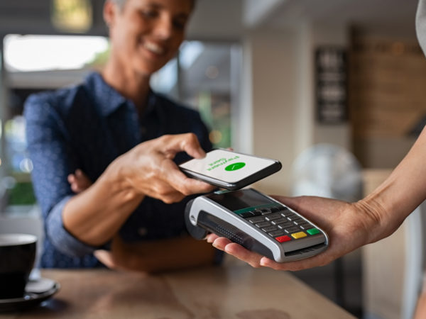 Woman paying bill through smartphone using NFC technology in a restaurant. Satisfied customer paying through mobile phone using contactless technology. Closeup hands of mobile payment at a coffee shop